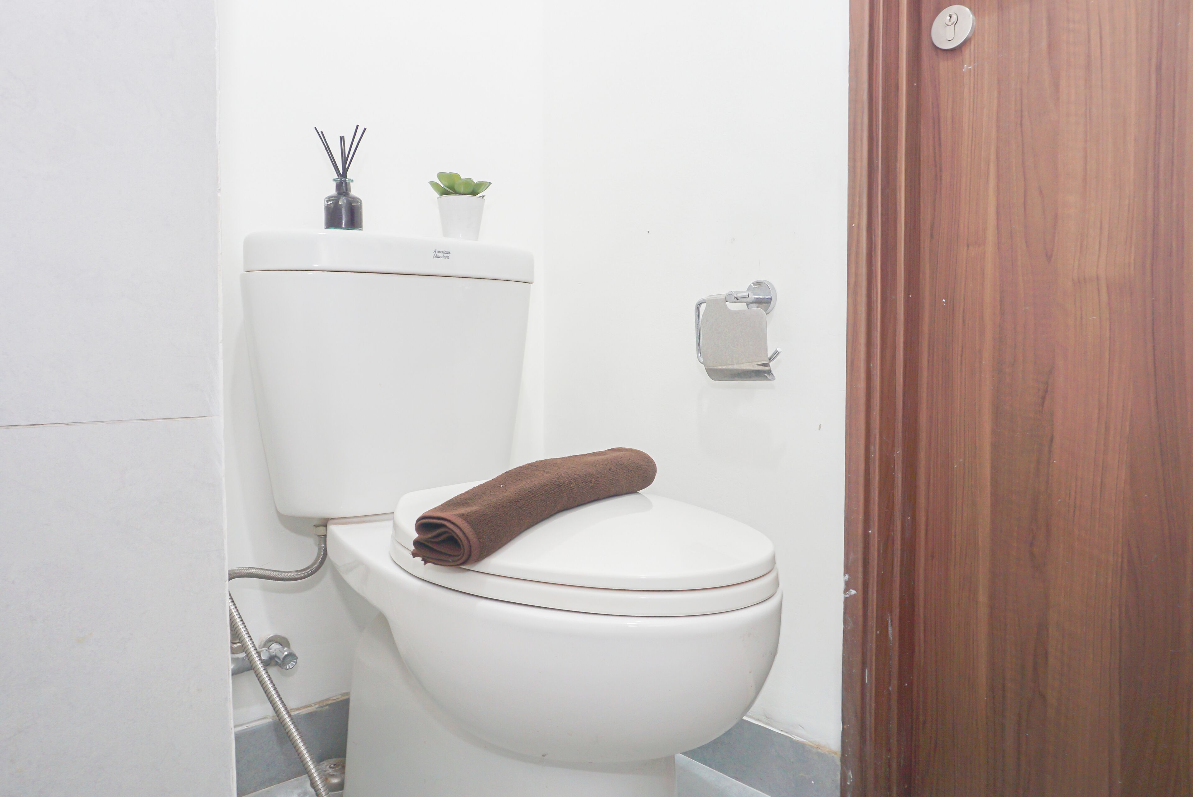 A white toilet with a brown towel on the lid, a small plant on the tank, and a toilet paper holder on the wall.