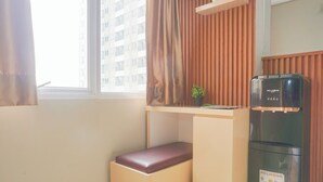 Una habitación pequeña con ventana, un escritorio con planta, dispensador de agua y un banco.