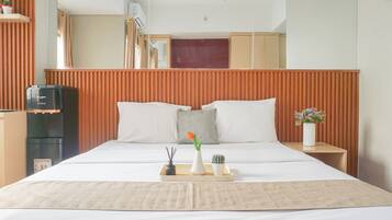 A hotel room with a large bed, a wooden headboard, a small table with a tray, and a refrigerator.