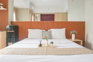 Habitación de hotel con una cama grande, un cabecero de madera, una mesita con bandeja y un refrigerador.