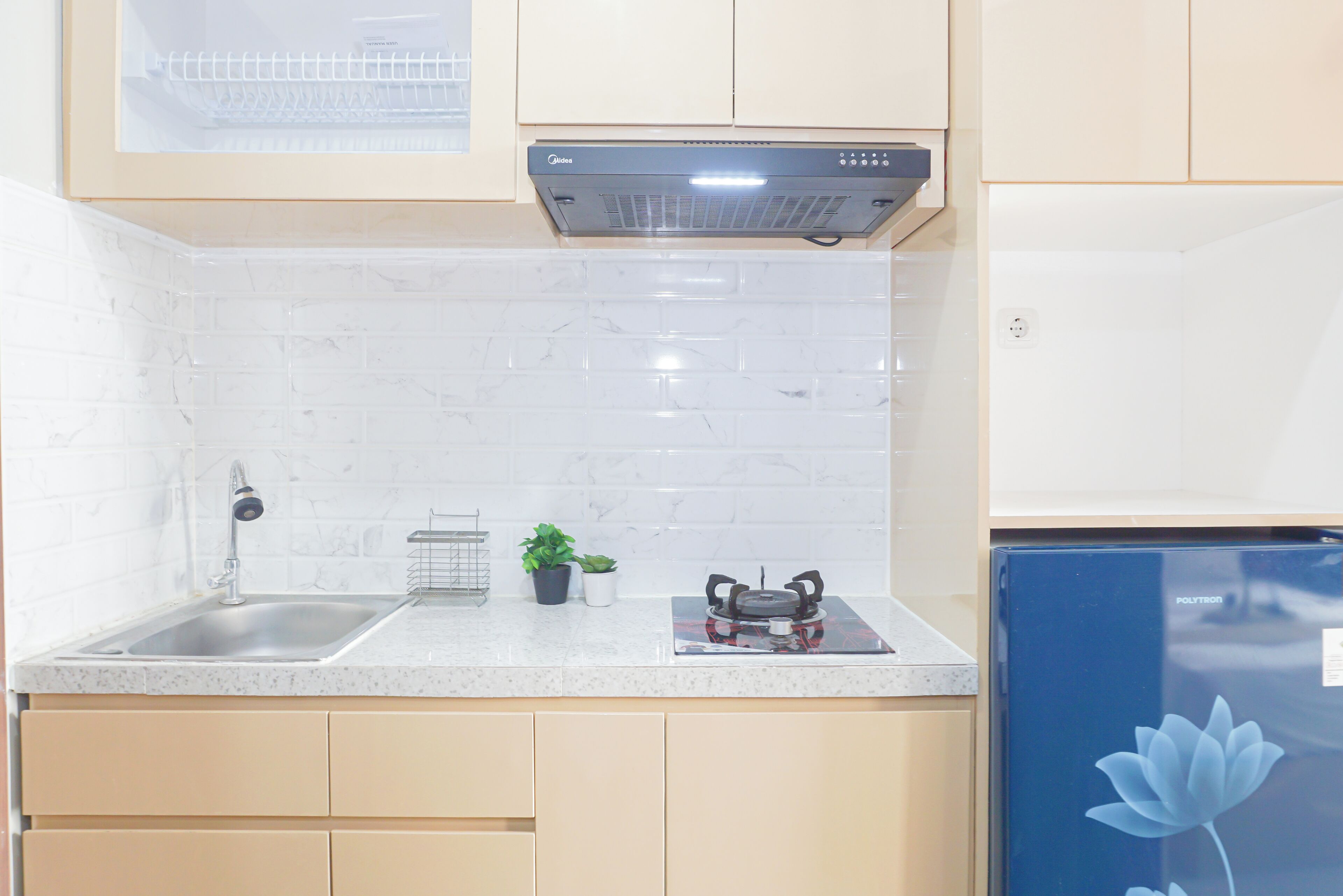 A kitchen with a stainless steel sink, a black range hood, and a small potted plant on the countertop.