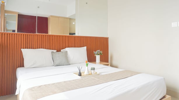 Habitación de hotel con cama, mesita de noche, espejo y cabecero de madera.