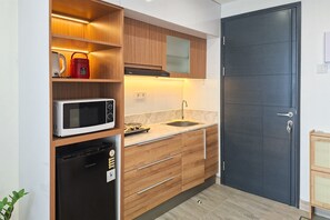 Une cuisine de taille réduite, avec des meubles de rangement en bois, un four à micro-ondes, un évier et une porte noire.