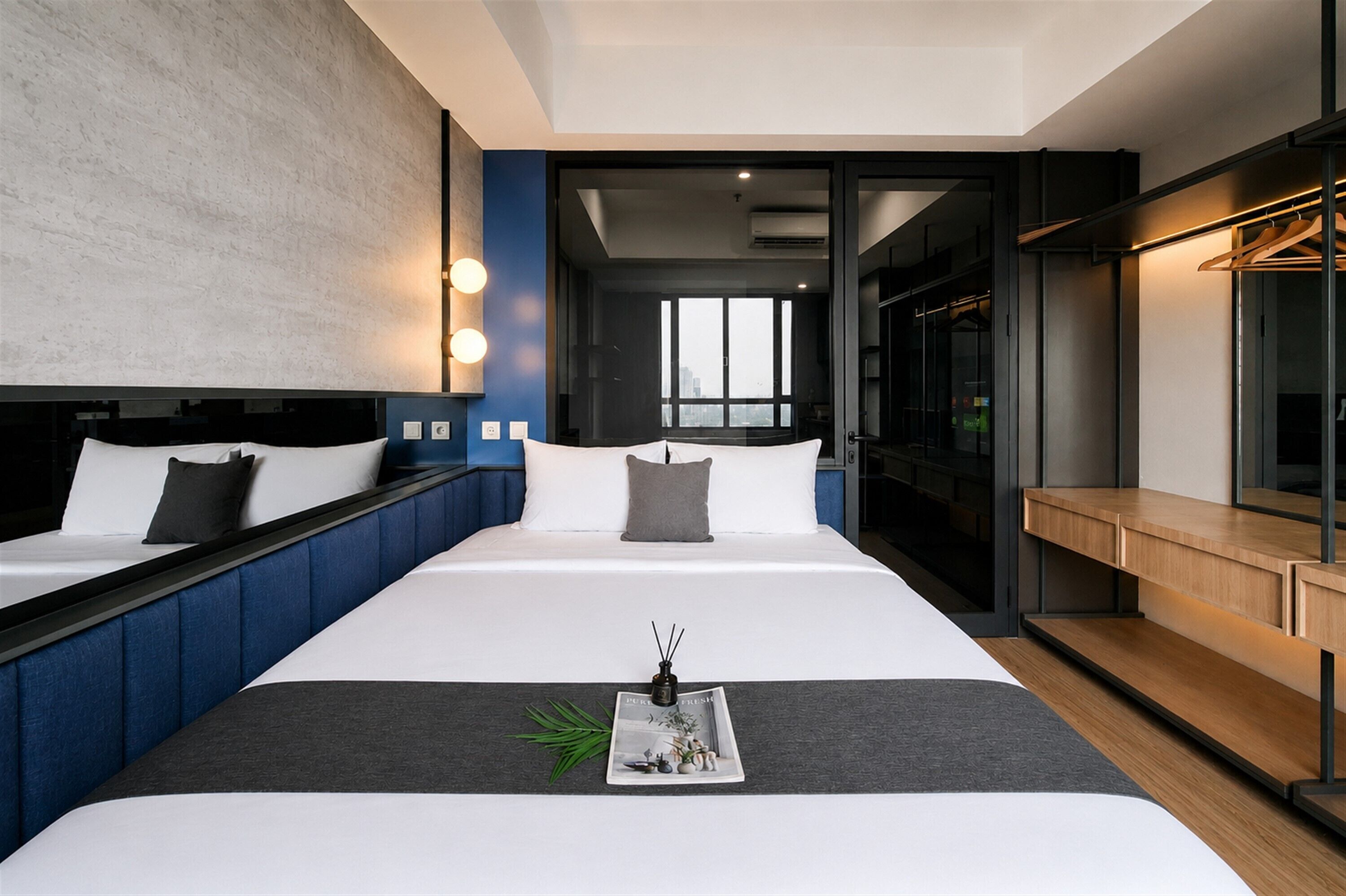 Una habitación de hotel moderna con una cama grande, mesitas de noche, vistas a la ciudad y un vestidor.