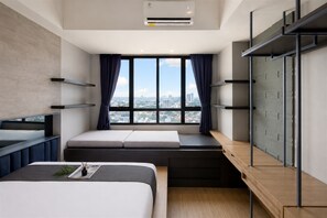 A modern hotel room with a bed, a desk, a window with a city view, and built-in shelves. - Chic With Urban Design 1Br Apartment At Collins Boulevard (Tangerang)
