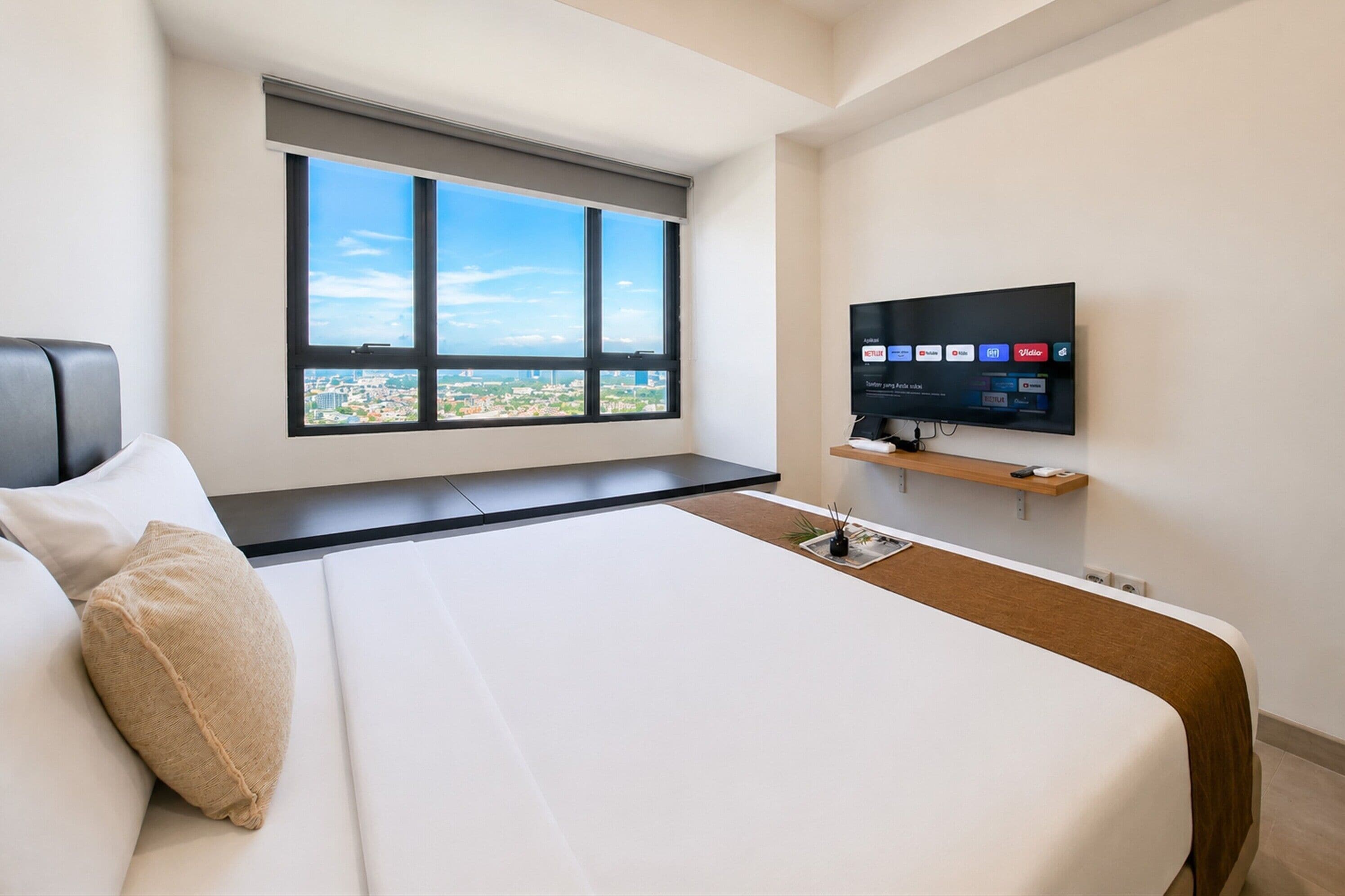 A hotel room with a large bed, a television mounted on the wall, and a window with a city view.