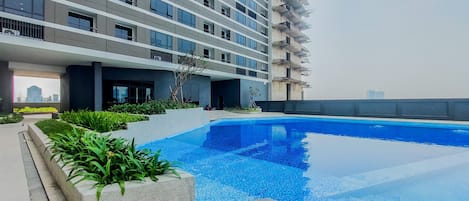 Un edificio moderno con piscina, rodeado de vegetación y un cielo despejado.