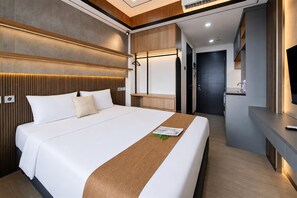 A modern hotel room with a large bed, wooden headboard, and a built-in TV. - Chic And Warm Studio Room At Apartment Collins Boulevard (Tangerang)
