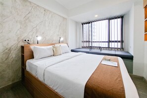 A modern hotel room with a marble wall, a large bed with a wooden headboard, bedside lamps, a window with blinds, and a built-in bench. - Great Deal Studio At Apartment Collins Boulevard (Tangerang)