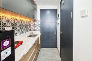A narrow kitchen with a dark door, a sink, and a countertop with a decorative backsplash. - Great Deal Studio At Apartment Collins Boulevard (Tangerang)