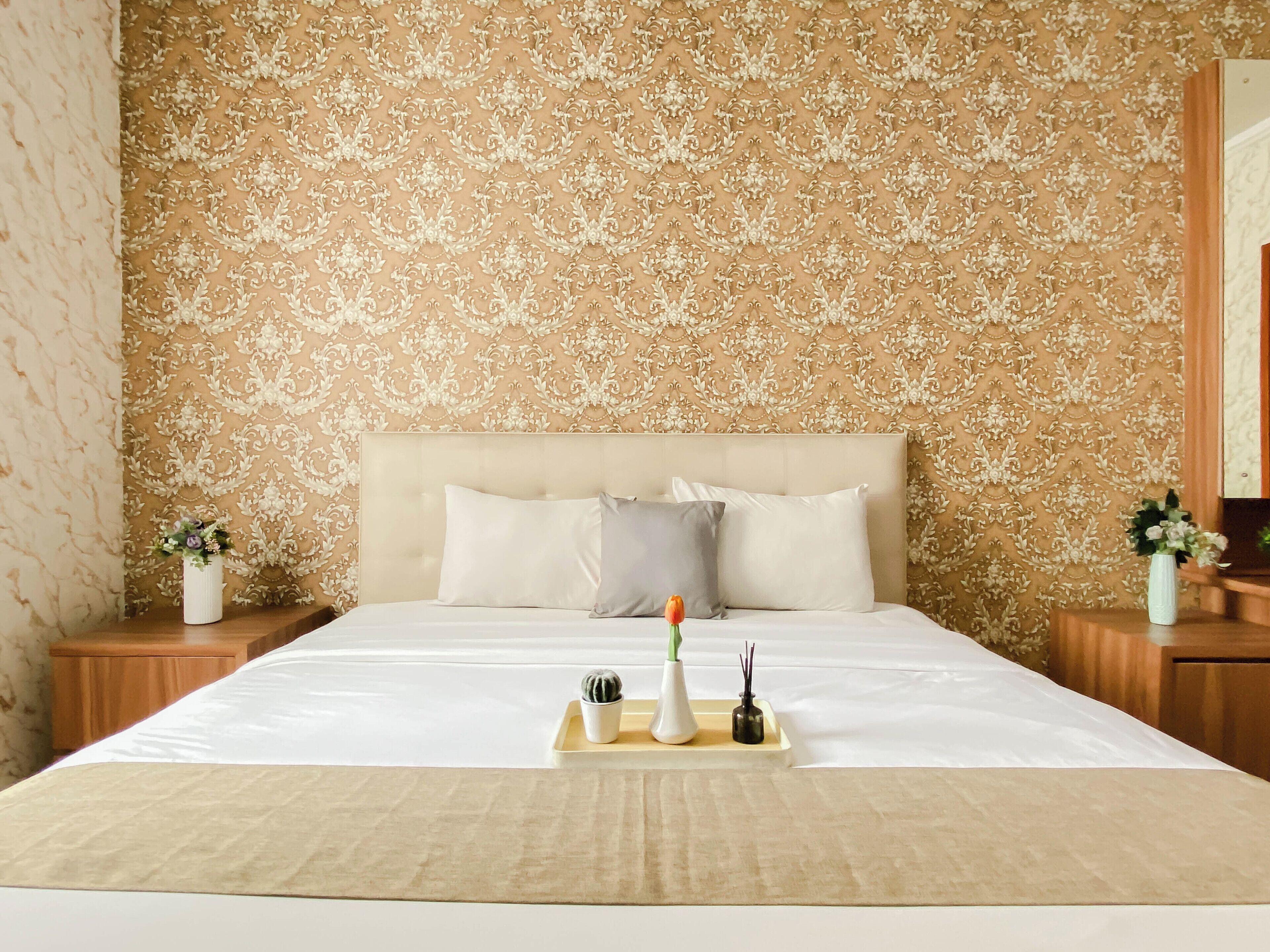 A neatly made bed with a white comforter, a beige headboard, and two bedside tables with vases of flowers.