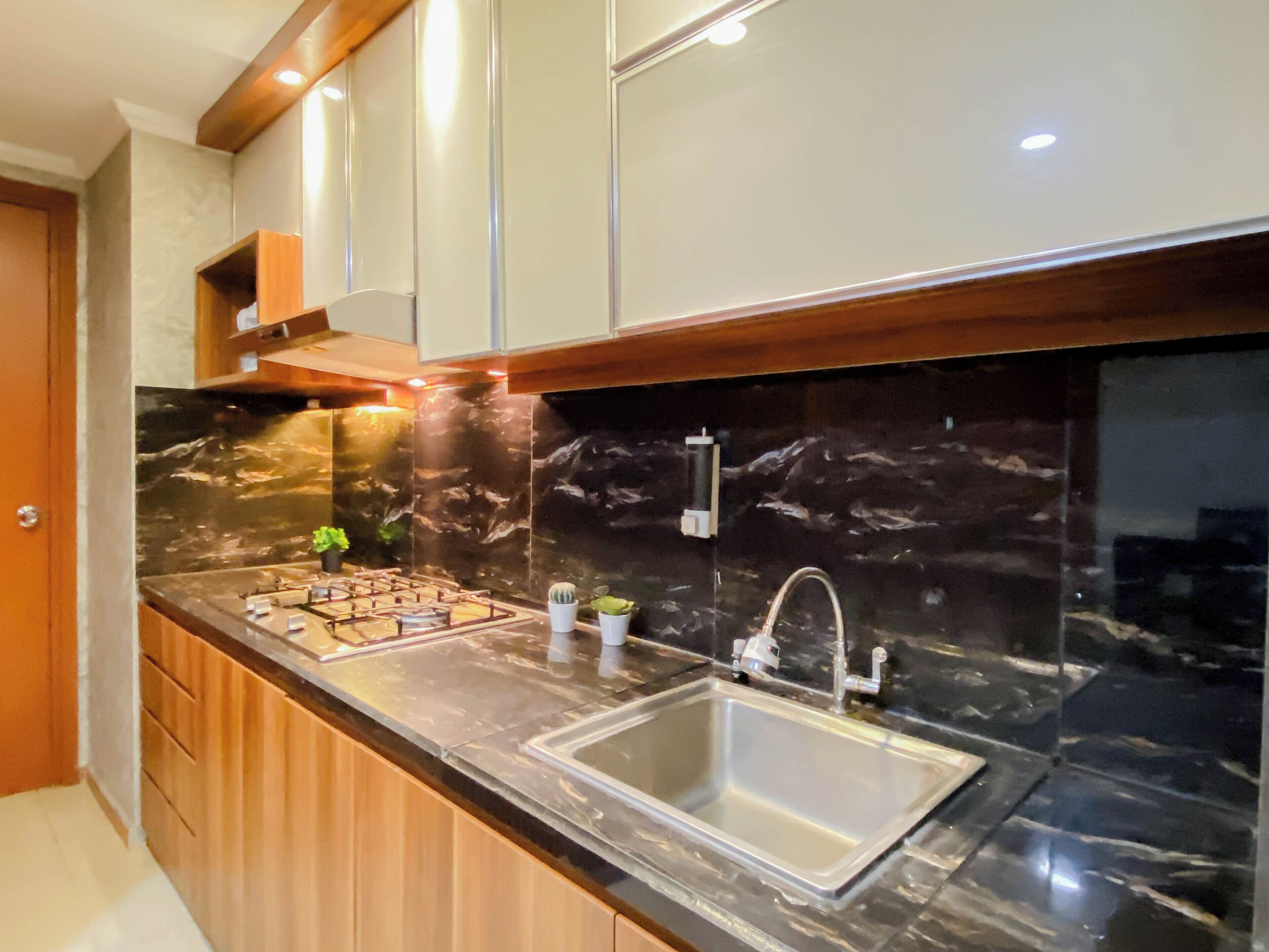 A modern kitchen with a marble countertop, stainless steel sink, wooden cabinets, and under-cabinet lighting.