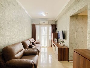 A living room with a brown leather sofa, a wooden cabinet, and a flat-screen TV. - Classic And Strategic 3Br At Apartment Grand Palace Kemayoran (Jakarta)
