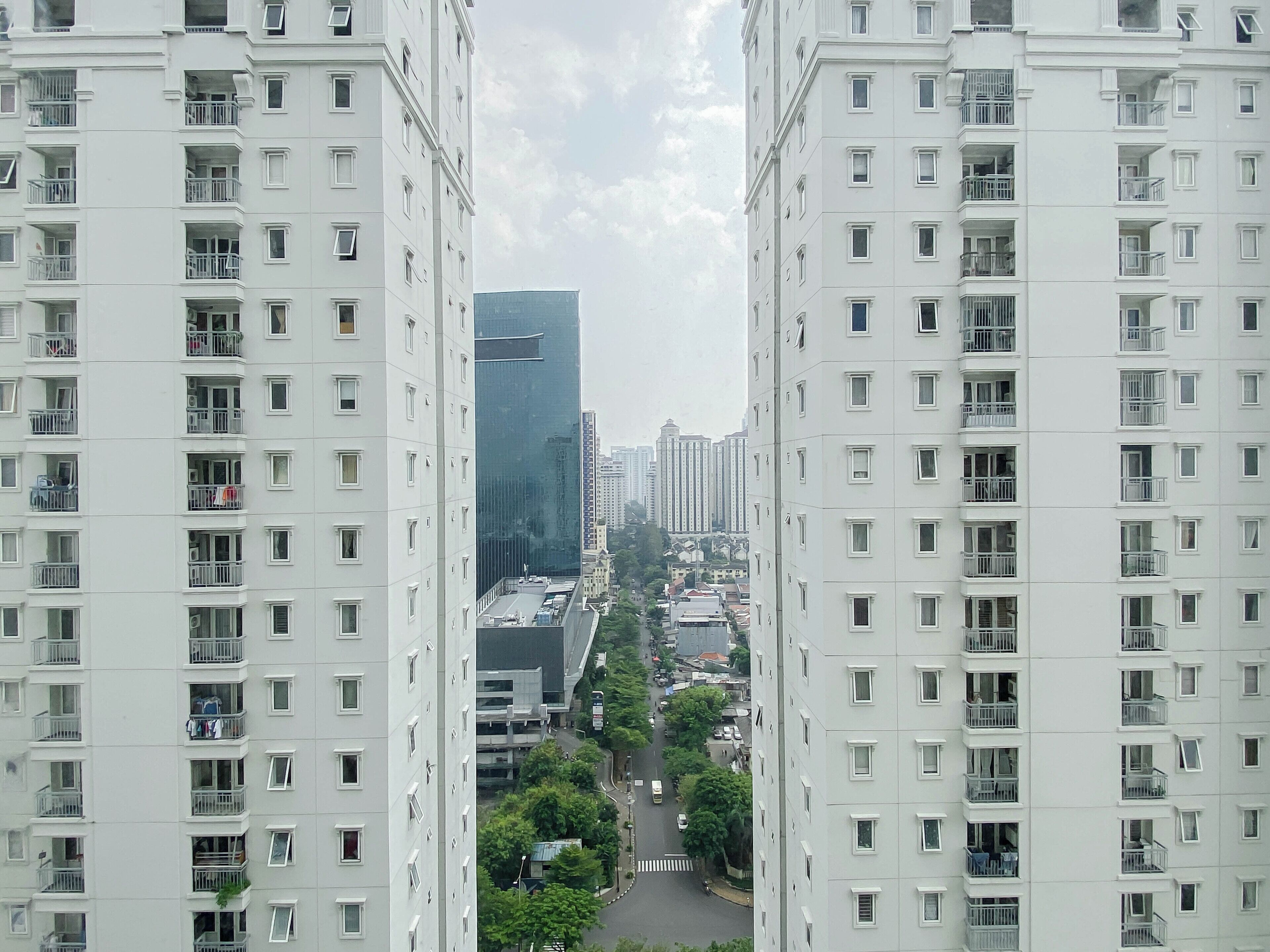 A high-rise residential building with multiple balconies, a central courtyard, and a view of surrounding high-rise buildings.