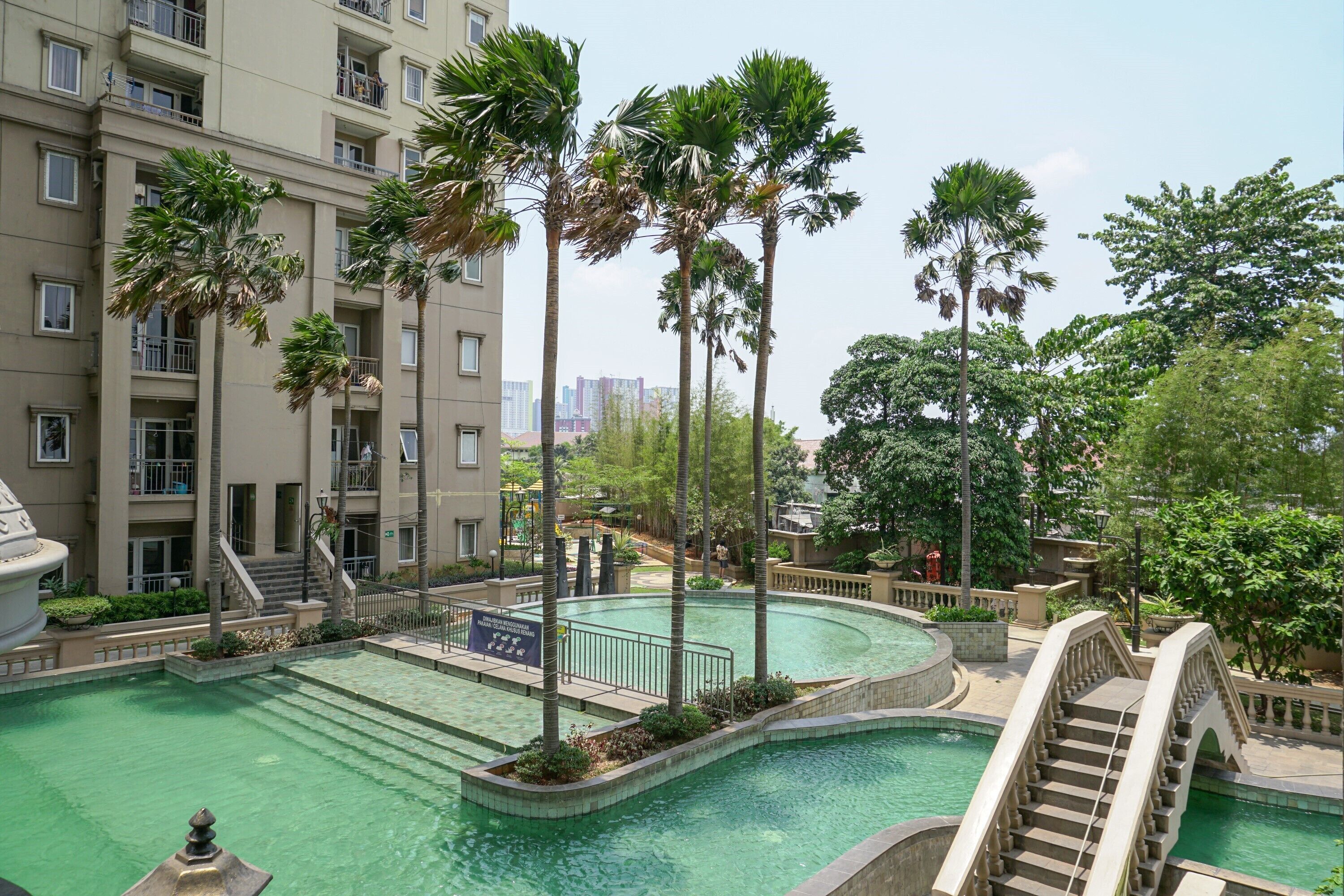 A swimming pool surrounded by palm trees and a multi-story building with balconies.
