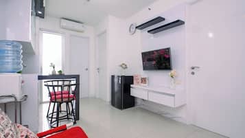 Una sala moderna con un sofá, un comedor con una silla, un refrigerador negro, un televisor montado en la pared y un dispensador de agua.