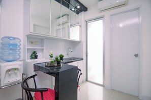A compact kitchen with a water dispenser, a sink, a chair, and a door. - Homey 2Br With Modern Interior At Apartment Bassura City (Jakarta)