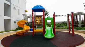 Un parque infantil con un tobogán amarillo, otro verde y una estructura para escalar.
