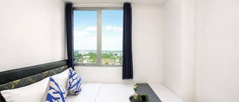 Una habitación de hotel con cama, ventana con cortinas, una mesita con una planta y aire acondicionado instalado en la pared.