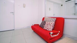 A red sofa with patterned cushions in a room with white walls and a large mirror. - Homey 2Br With Modern Interior At Apartment Bassura City (Jakarta)