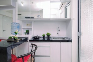A modern kitchen with white cabinets, a black countertop, a sink, a clock, and a water dispenser. - Homey 2Br With Modern Interior At Apartment Bassura City (Jakarta)