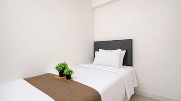 Una cama individual con cabecera oscura, ropa de cama blanca y dos pequeñas macetas sobre un posavasos redondo.