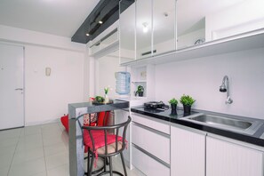 A modern kitchen with a black countertop, stainless steel sink, and a red chair with a polka dot cushion. - Homey 2Br With Modern Interior At Apartment Bassura City (Jakarta)