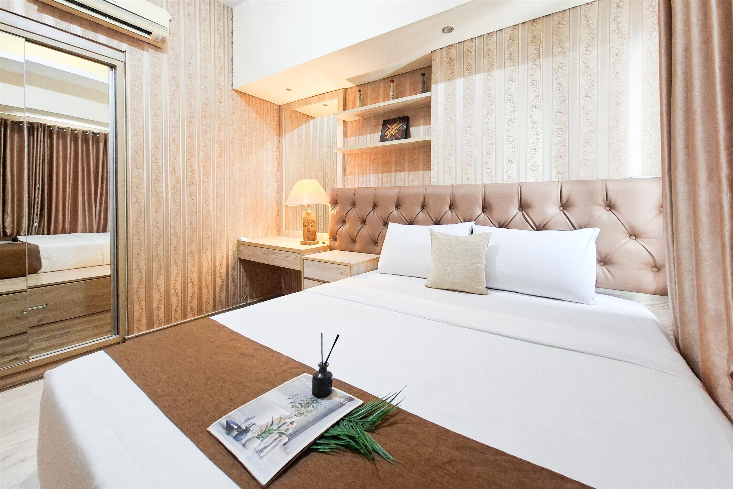A hotel room with a large bed, a bedside table with a lamp, a mirror, and a wardrobe.