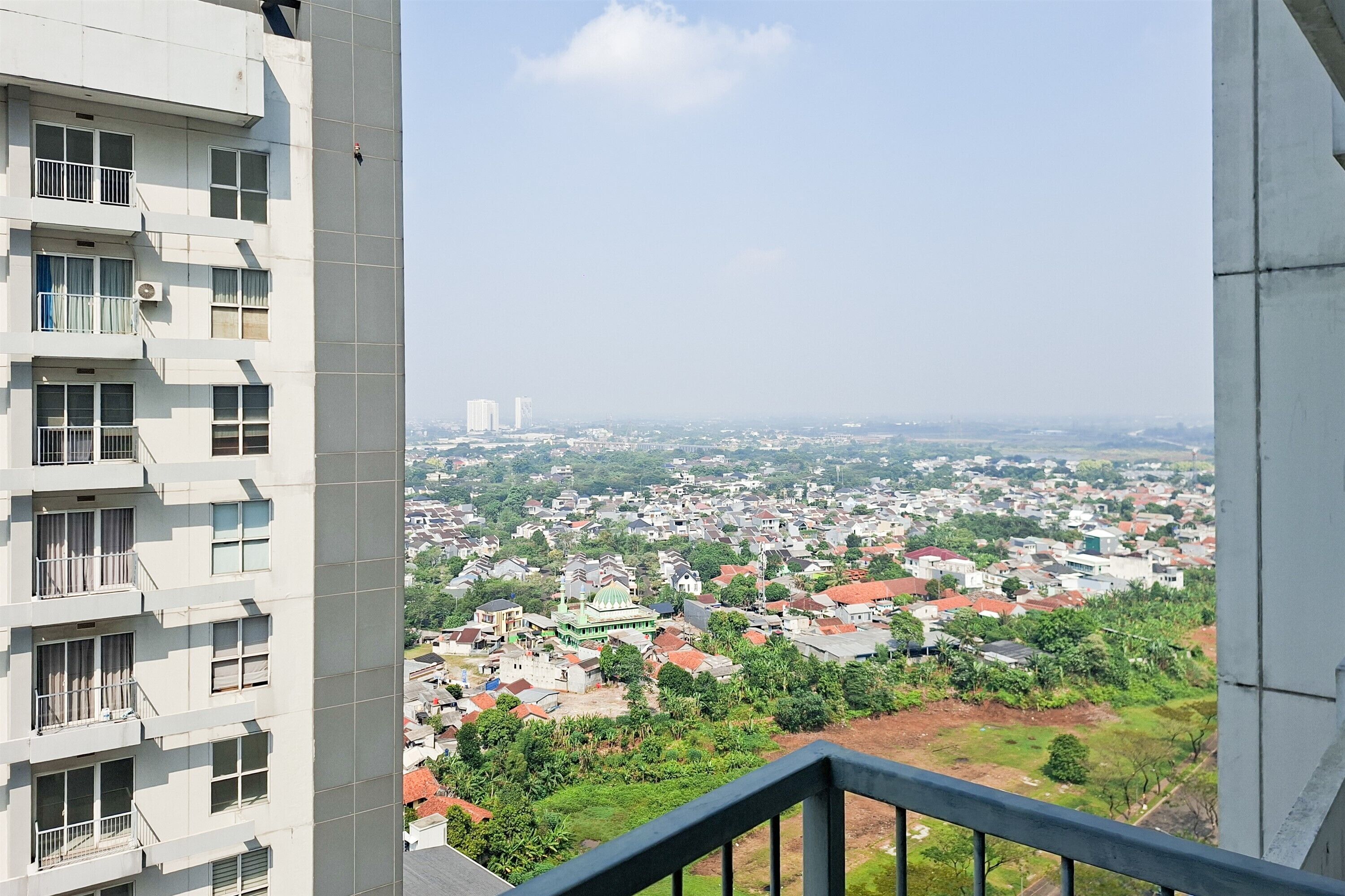 Um edifício alto com várias varandas e vista para uma área residencial com casas e vegetação.