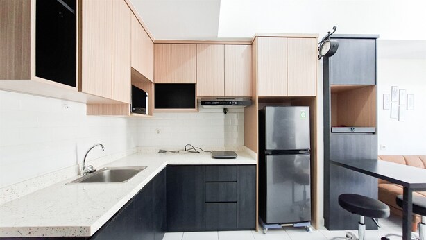 A modern kitchen with a built-in microwave, a stainless steel refrigerator, and a black countertop. - Clean And Nice 1Br At Apartment Casa De Parco (Tangerang)