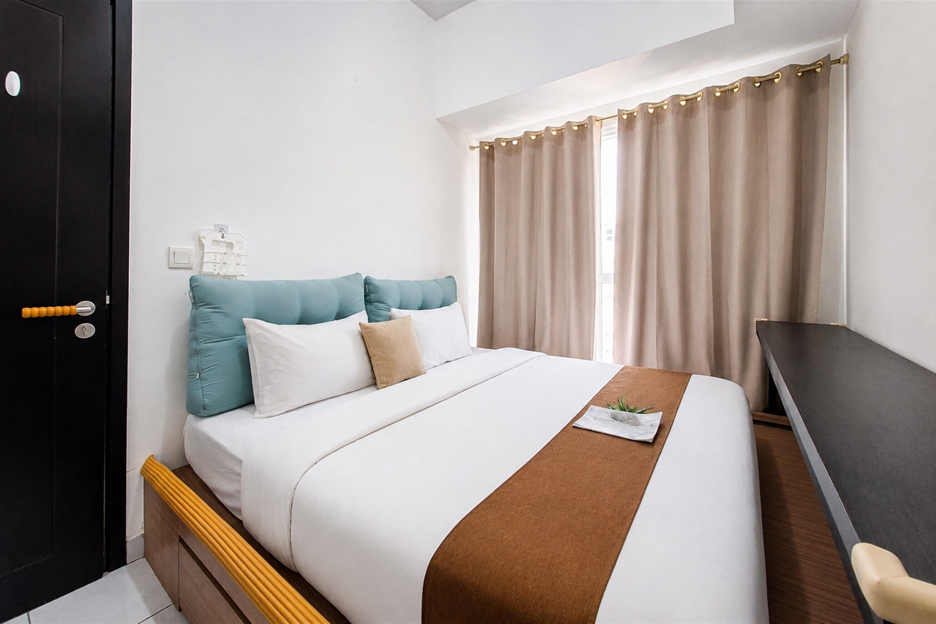A hotel room with a bed, a desk, and a window with curtains.