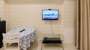 Ein Hotelzimmer mit Bett, einem Sessel, einem an der Wand befestigten Fernseher und einem kleinen Tisch.