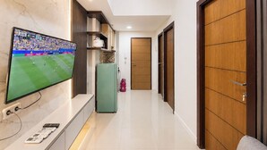 A hallway with a TV displaying a sports event, a green cabinet, and a fire extinguisher. - Functional With Minimalist Design 2Br At Vida View Makassar Apartment (Makassar)