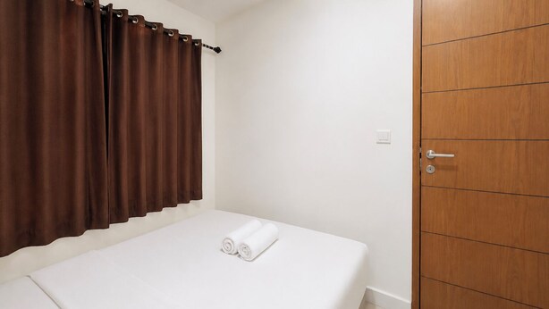 A single bed with white bedding, a brown curtain, and a wooden wardrobe. - Functional With Minimalist Design 2Br At Vida View Makassar Apartment (Makassar)