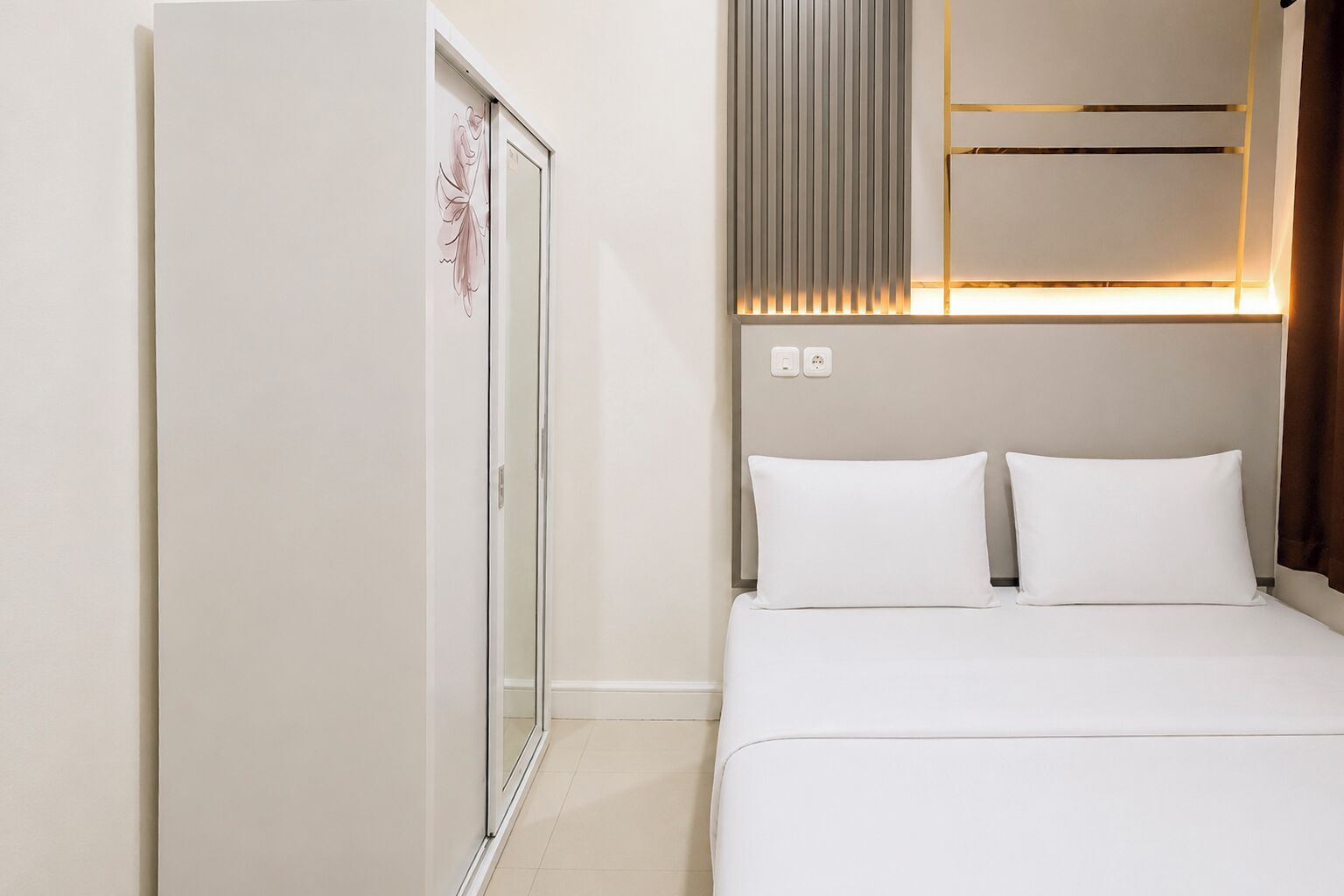 A hotel room with a bed, a wardrobe, a wall-mounted air conditioning unit, and a power outlet.