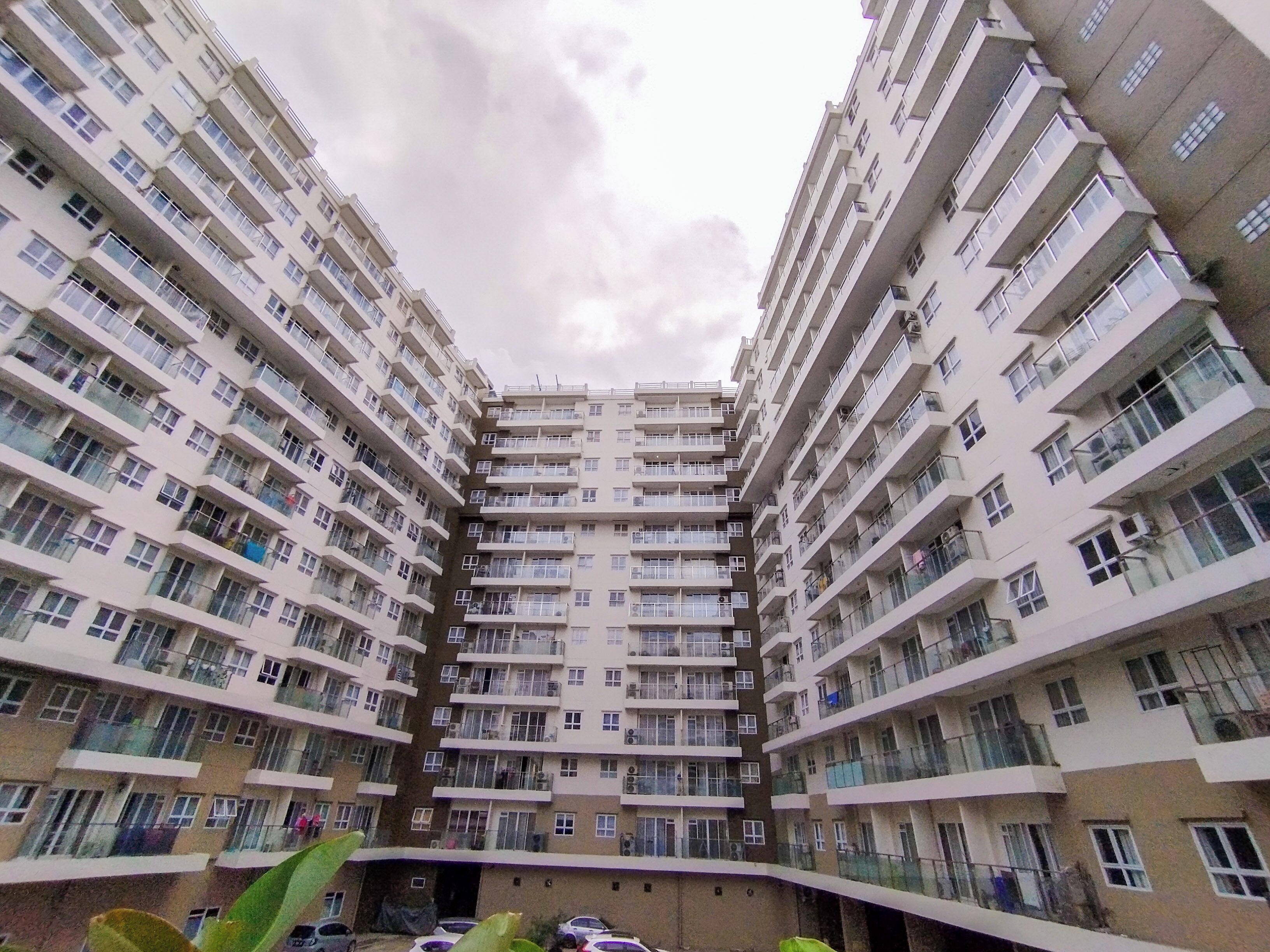 A multi-story residential building with balconies, a central courtyard, and parked cars.