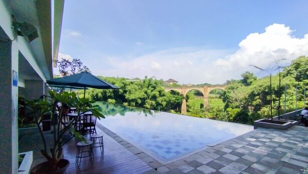 Ein Fernblick vom Infinity-Pool auf eine Brücke, umgeben von Grün und wolkenlosem Himmel.