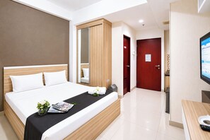 Ein Hotelzimmer mit Bett, Fernseher, Schreibtisch und einer Badezimmertür.