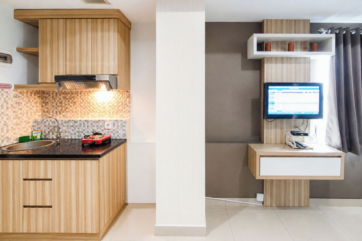 Una cocina moderna con armarios de madera, horno empotrado, un lavabo y un televisor de pantalla plana montado en un estante de madera.