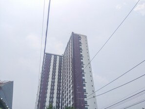 A tall, multi-story building with a modern architectural design, featuring a series of balconies and windows. - Studio Apartment At Dave Near University Of Indonesia (Ui) (Depok)