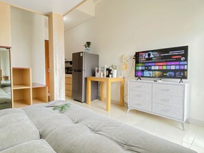 A modern living room with a sofa, a television, a small table with a vase, and a refrigerator. - Studio Apartment At Dave Near University Of Indonesia (Ui) (Depok)