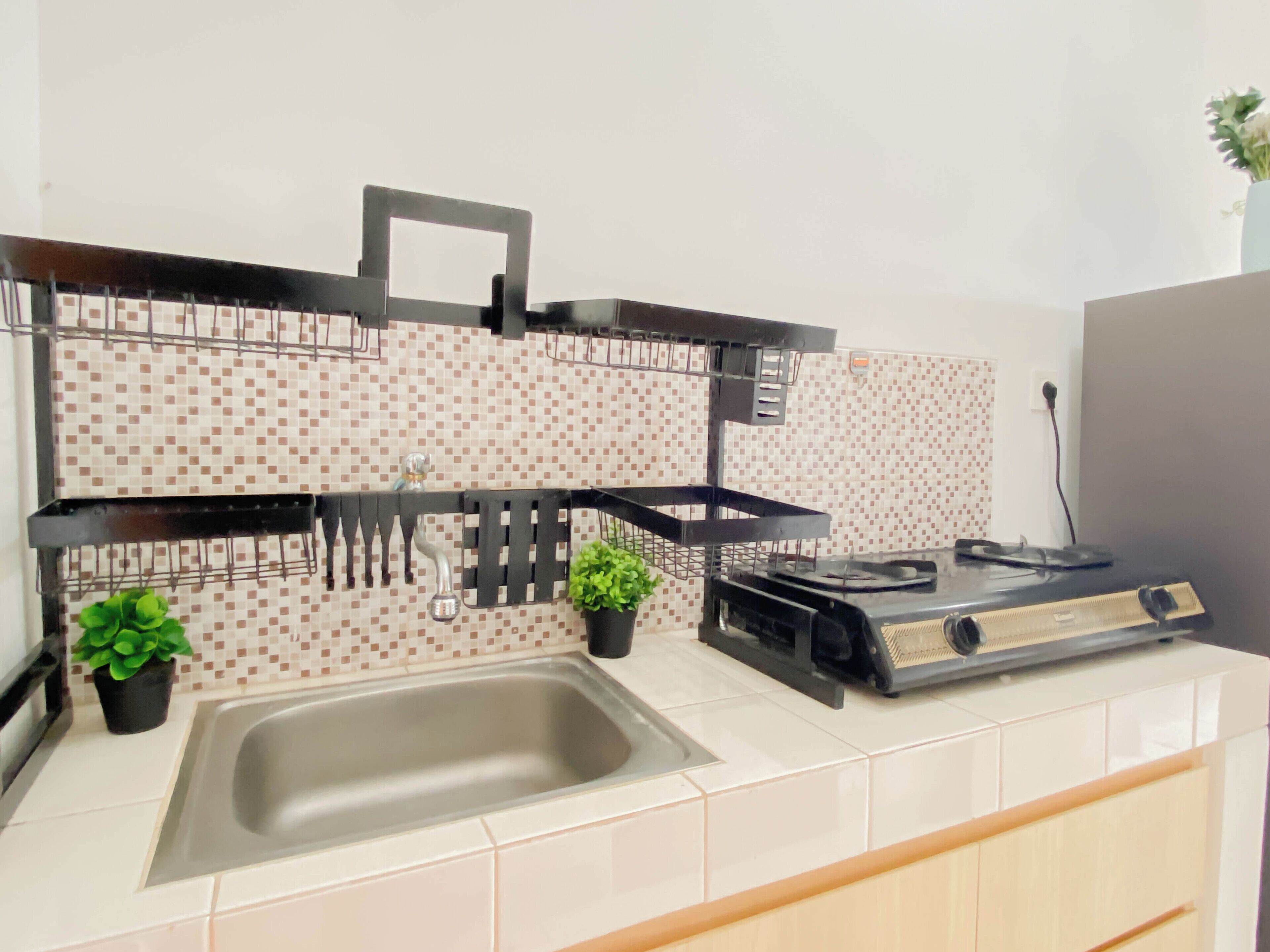 A kitchen with a tiled backsplash, a stainless steel sink, a stove, and a black metal rack.