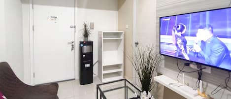 A living room with a flat-screen TV, a glass coffee table, a sofa, a white door, a white shelf, and a black cabinet.