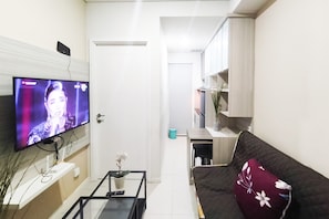 Ein Wohnzimmer mit Flachbildfernseher, einer Couch, einem Couchtisch und einer kleinen Pflanze.