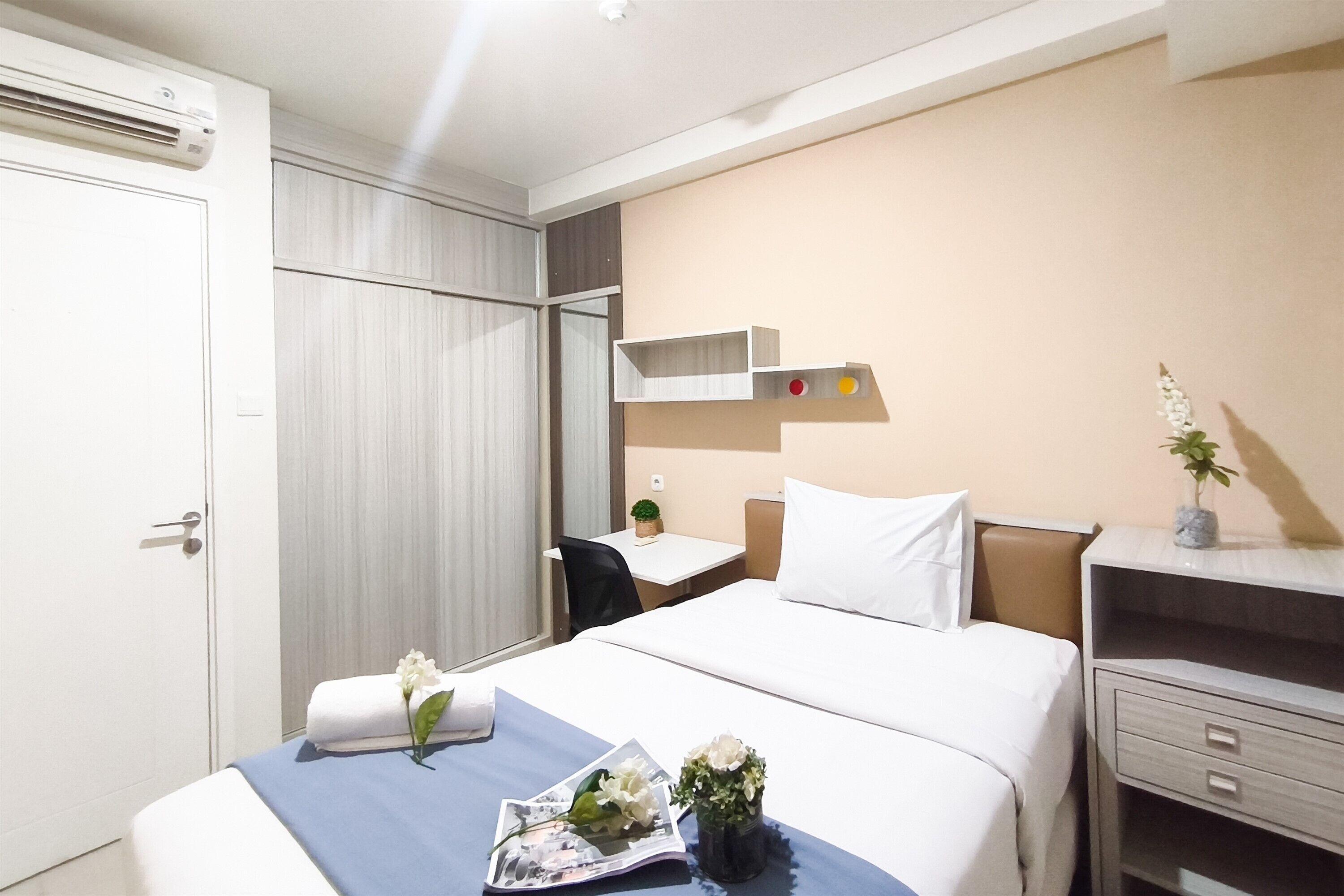Een hotelkamer met een bed, nachtkastje, bureau, stoel en een kleine potplant.
