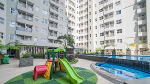 Un edificio residenziale con diversi balconi, un'area giochi per bambini con scivoli e una piscina.
