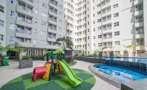 Ein Wohngebäude mit mehreren Balkonen, einem Spielplatz für Kinder mit Rutschen und einem Schwimmbad.