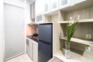 A compact kitchen with a black refrigerator, a small countertop, and a vase with green plants. - Practical Living In 1Br Room At Apartment Parahyangan Residence (Bandung)