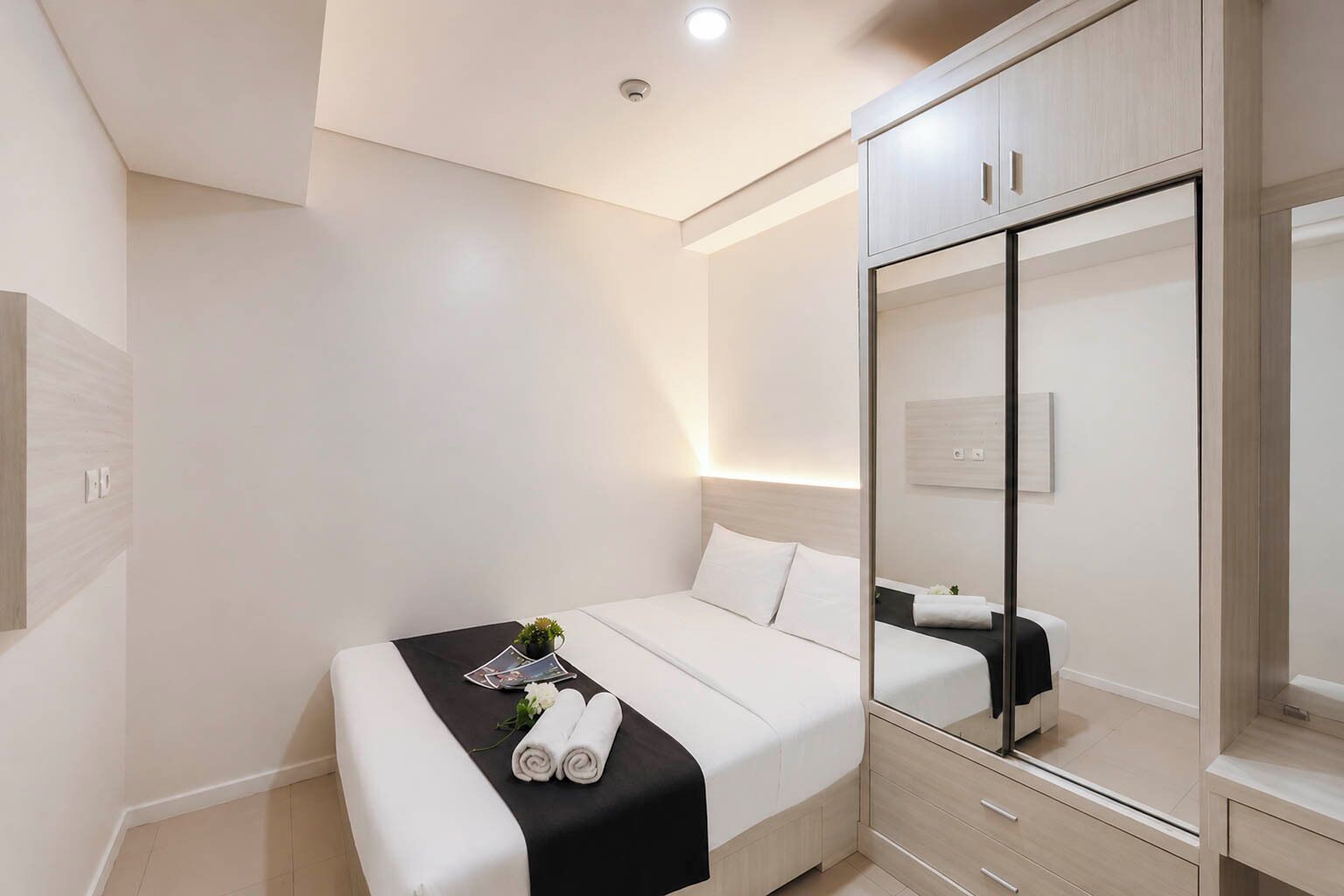 Ein modernes Hotelzimmer mit Bett, Spiegel, Kleiderschrank und Nachttisch.