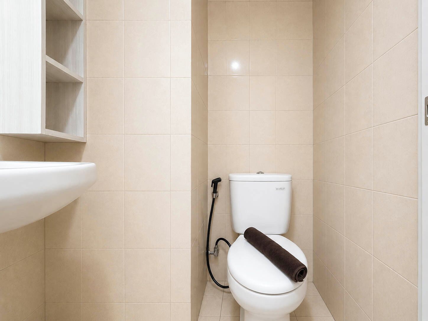 Ein Badezimmer mit einer weißen Toilette, beigen Fliesen und einem weißen Waschbecken.